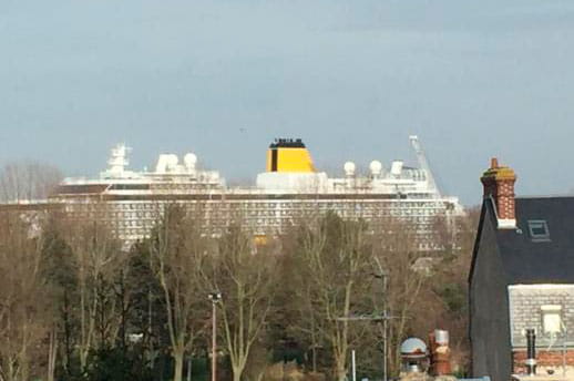 Spirit of Discovery's yellow funnel visible above the trees of Honfleur